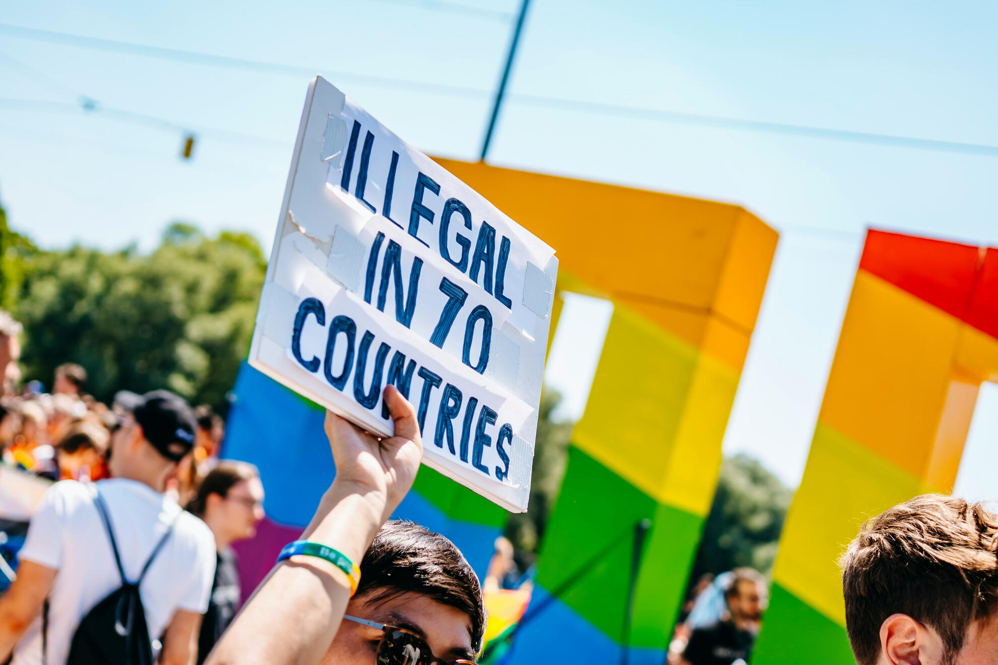 Queer pride costs Person holding up a sign during a queer pride march that reads "Illegal in 70 countries"